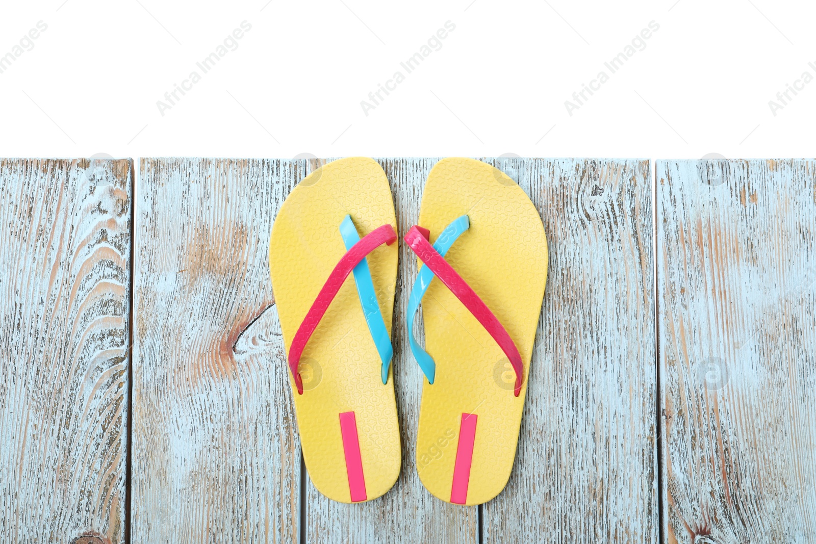 Photo of Yellow flip flops on light wooden table against white background, top view