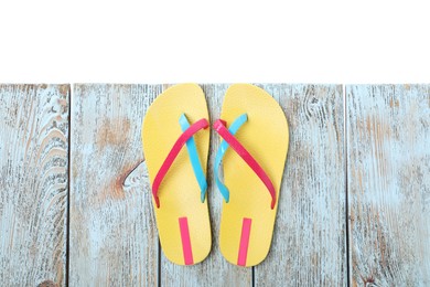 Yellow flip flops on light wooden table against white background, top view