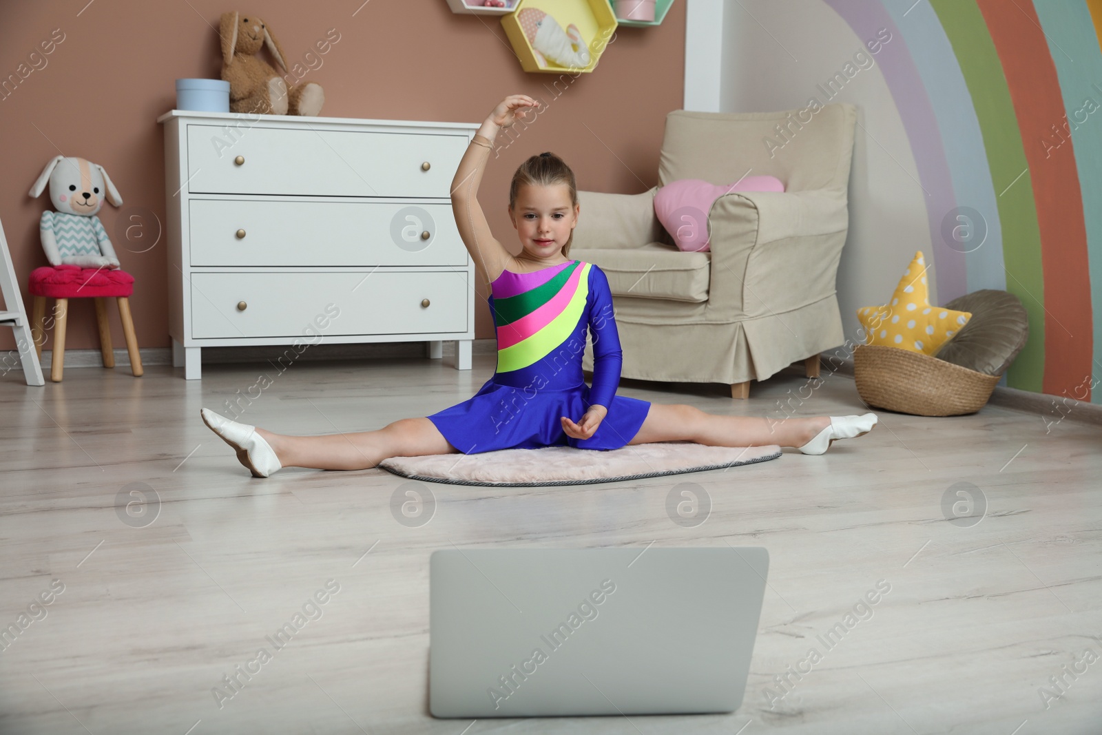 Photo of Cute little girl warming up before online dance class at home