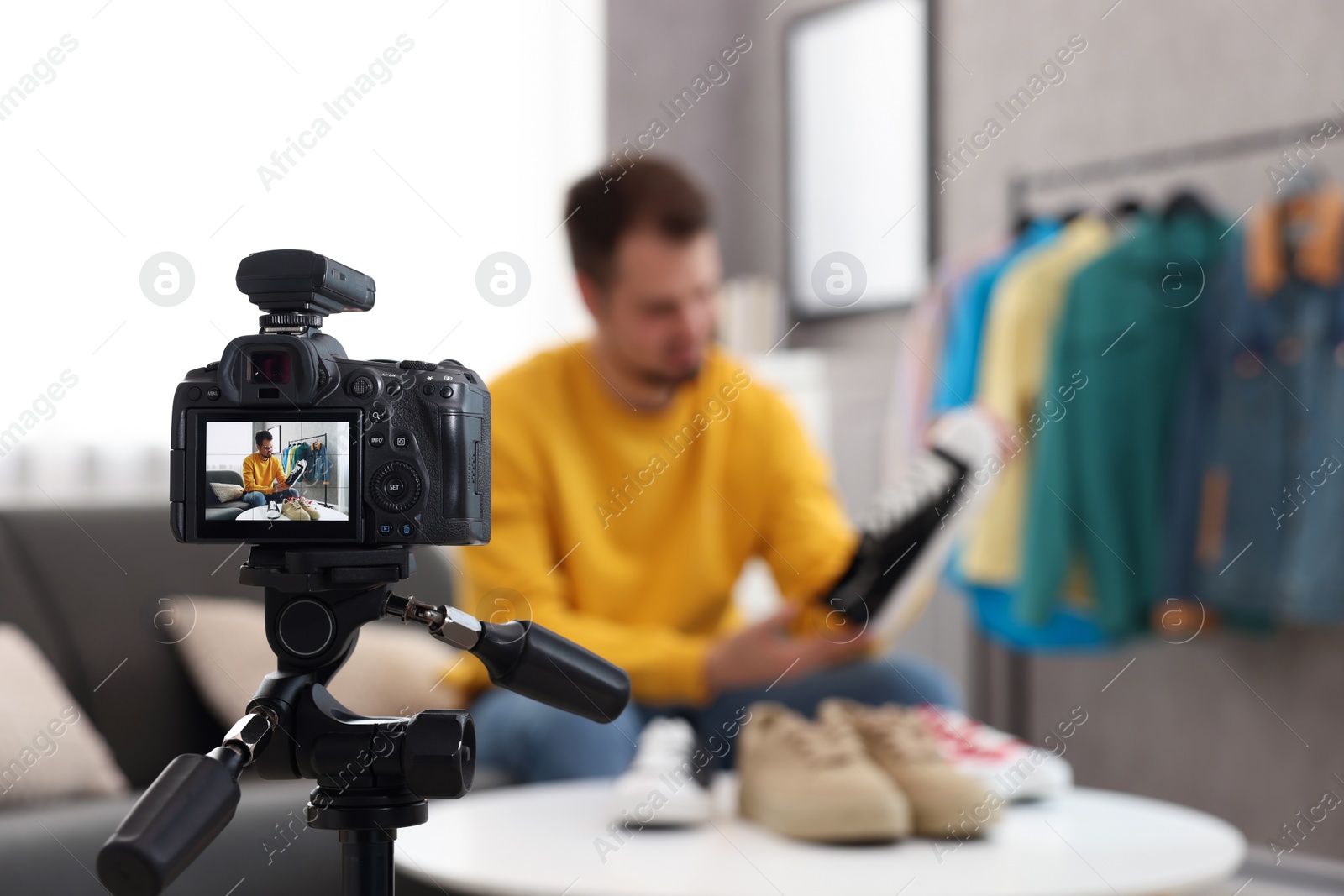 Photo of Fashion blogger looking at shoe while recording video at home, focus on camera