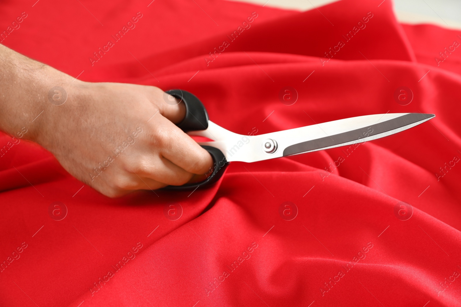 Photo of Professional tailor cutting red fabric with scissors in workshop, closeup