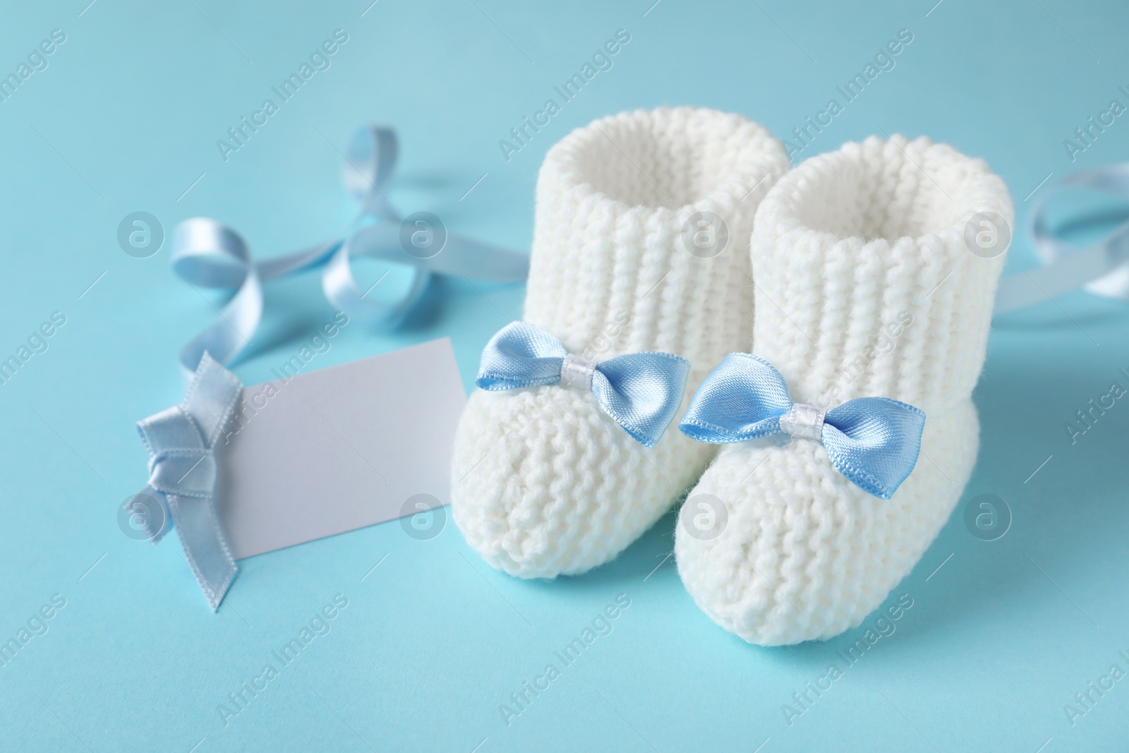 Photo of Handmade baby booties and empty greeting card on color background