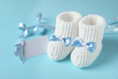 Handmade baby booties and empty greeting card on color background