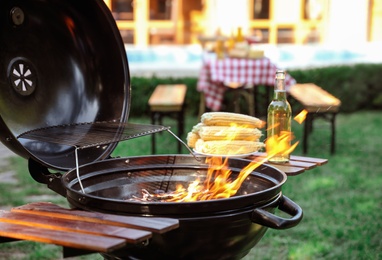 Barbecue grill with corn cobs and bottle of beer outdoors