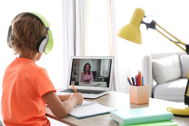 Photo of Little boy studying with teacher via video conference at home. Distance learning during COVID-19 pandemic