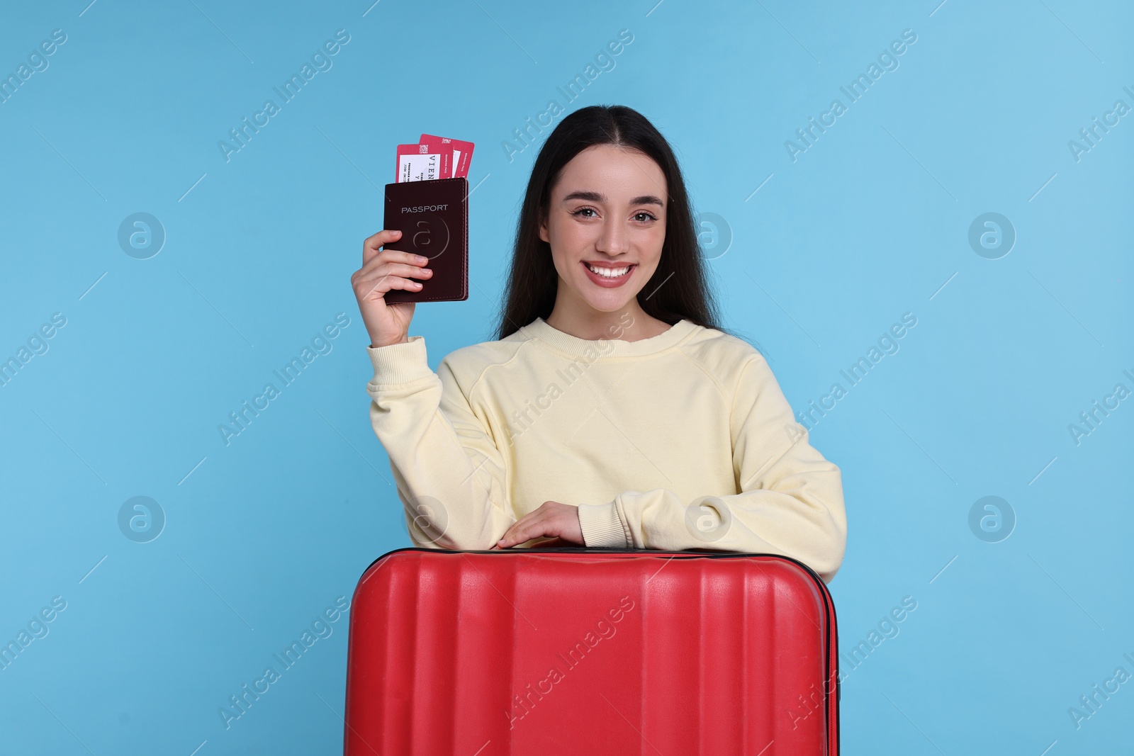 Photo of Smiling woman with passport, tickets and suitcase on light blue background