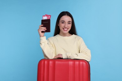 Photo of Smiling woman with passport, tickets and suitcase on light blue background