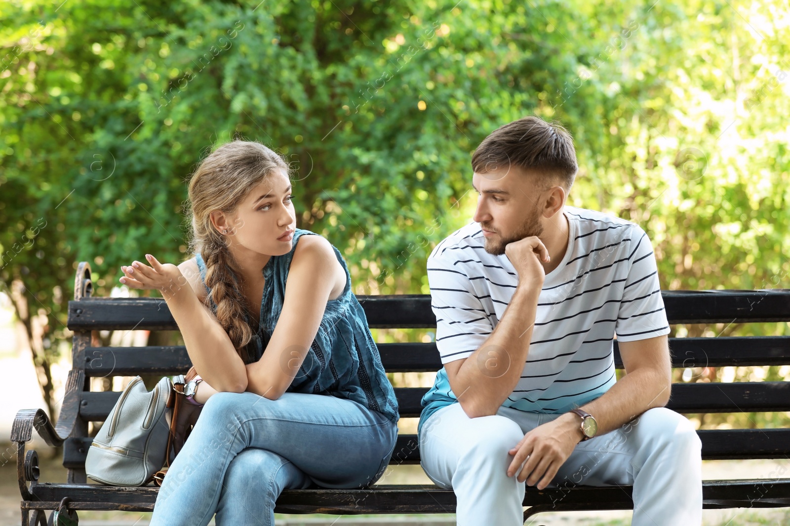 Photo of Young couple arguing while sitting on bench in park. Problems in relationship