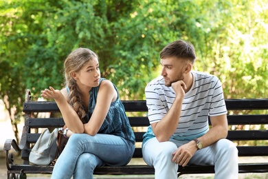 Photo of Young couple arguing while sitting on bench in park. Problems in relationship