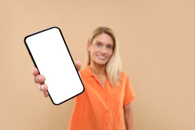Happy woman holding smartphone with blank screen on beige background, selective focus
