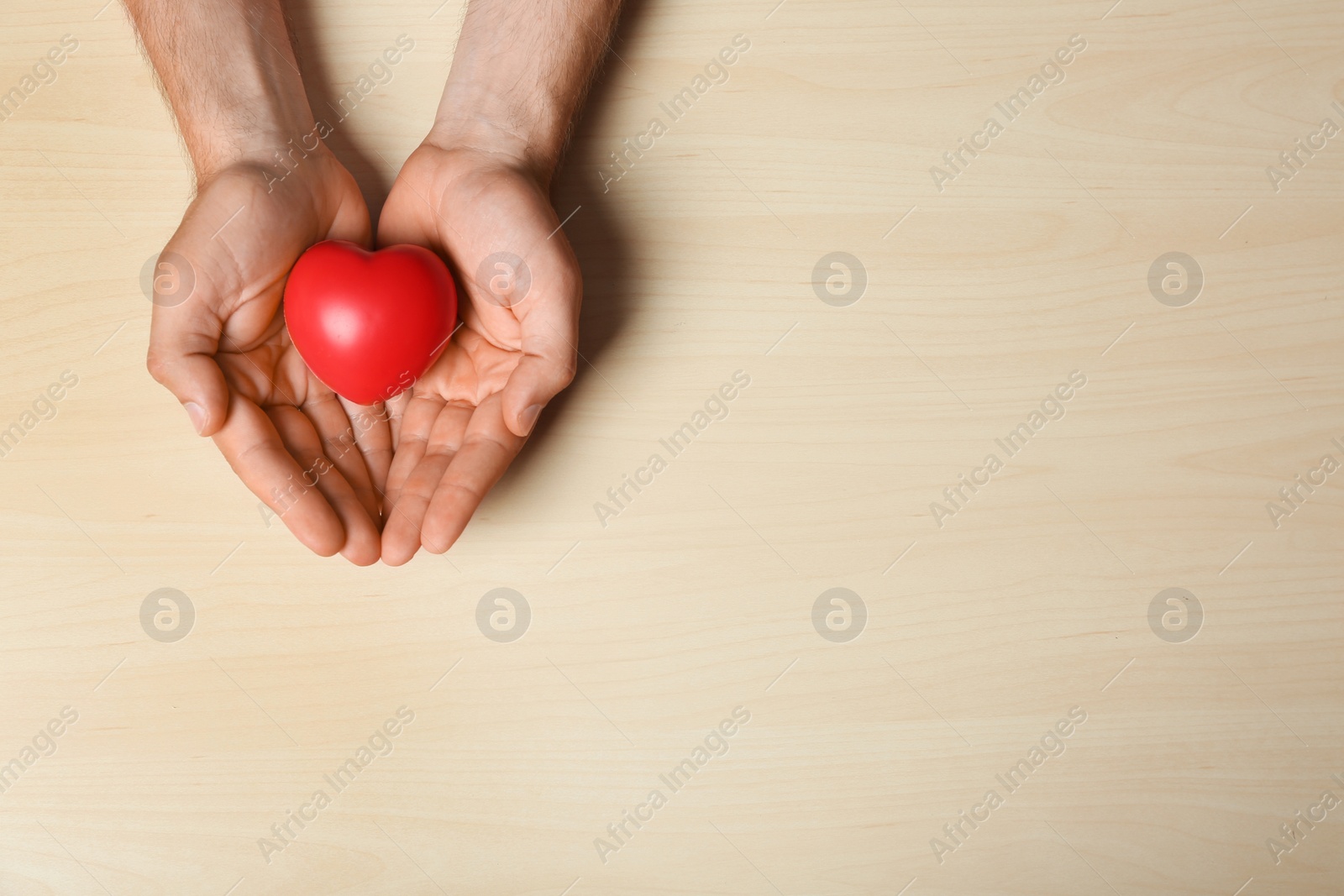 Photo of Young man holding red heart on light wooden background, top view with space for text. Donation concept