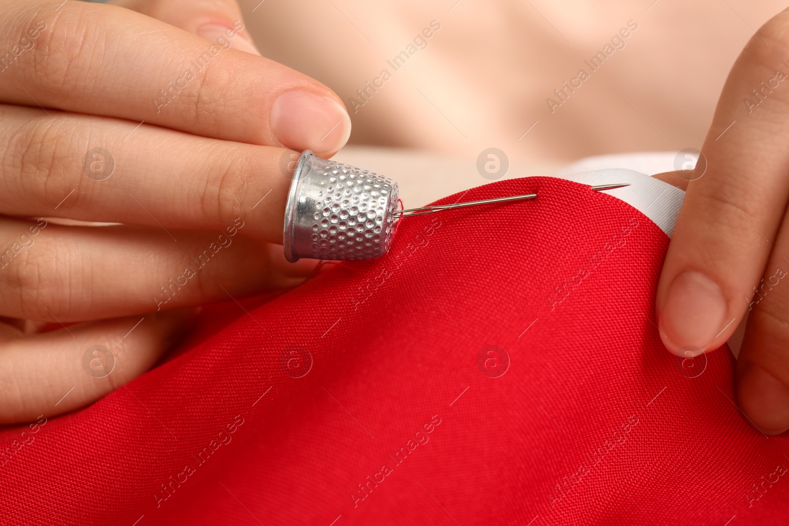 Photo of Woman sewing on red fabric with thimble and needle, closeup