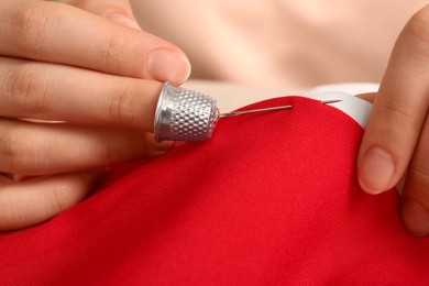 Photo of Woman sewing on red fabric with thimble and needle, closeup