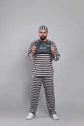 Prisoner in special uniform with mugshot letter board  
on grey background