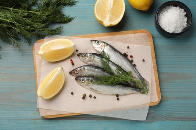 Photo of Fresh raw sprats, cut lemon, dill and spices on light blue wooden table, flat lay