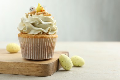 Tasty Easter cupcake with vanilla cream and candies on gray table, space for text