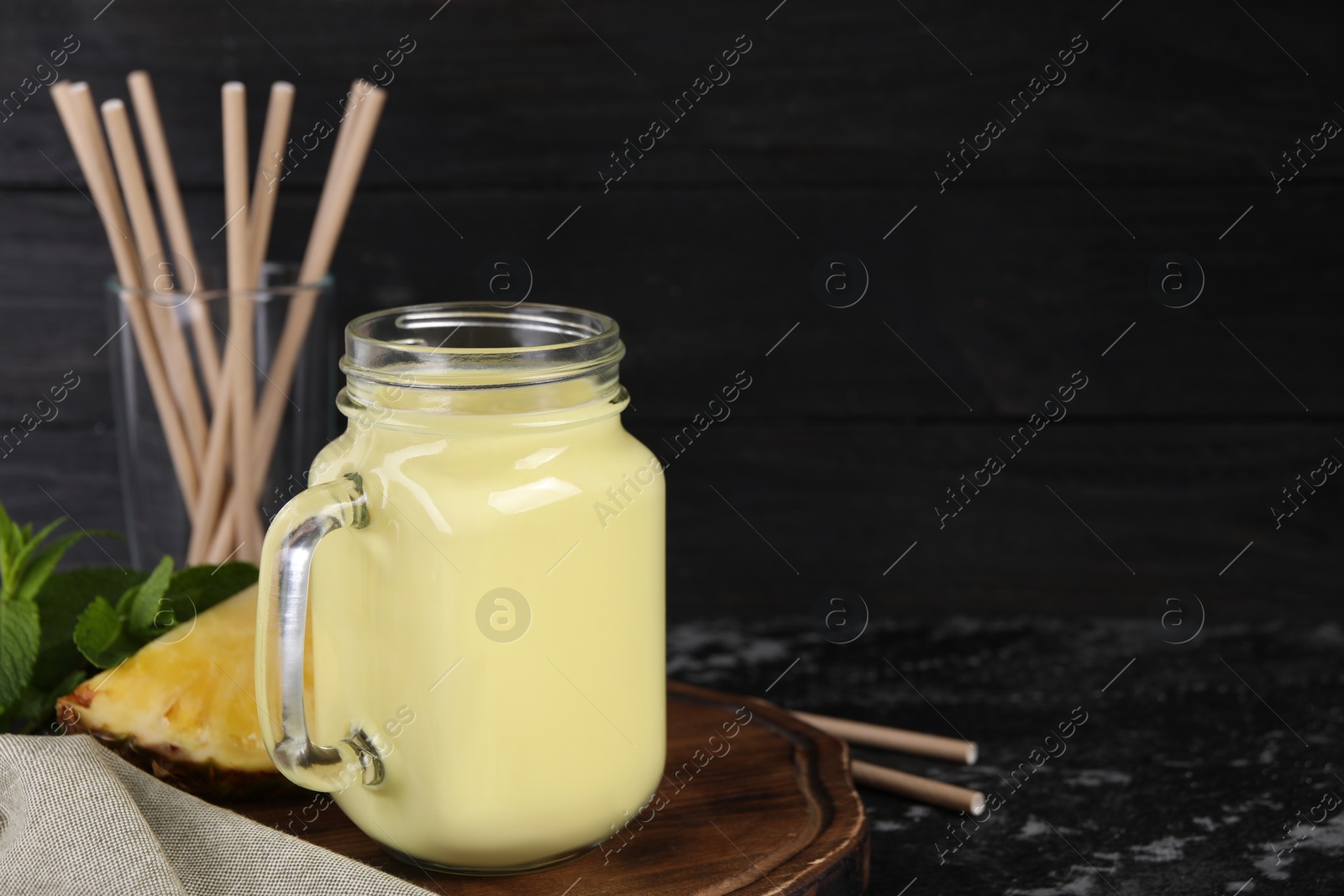 Photo of Tasty pineapple smoothie, mint, slice of fruit and straws on dark textured table. Space for text