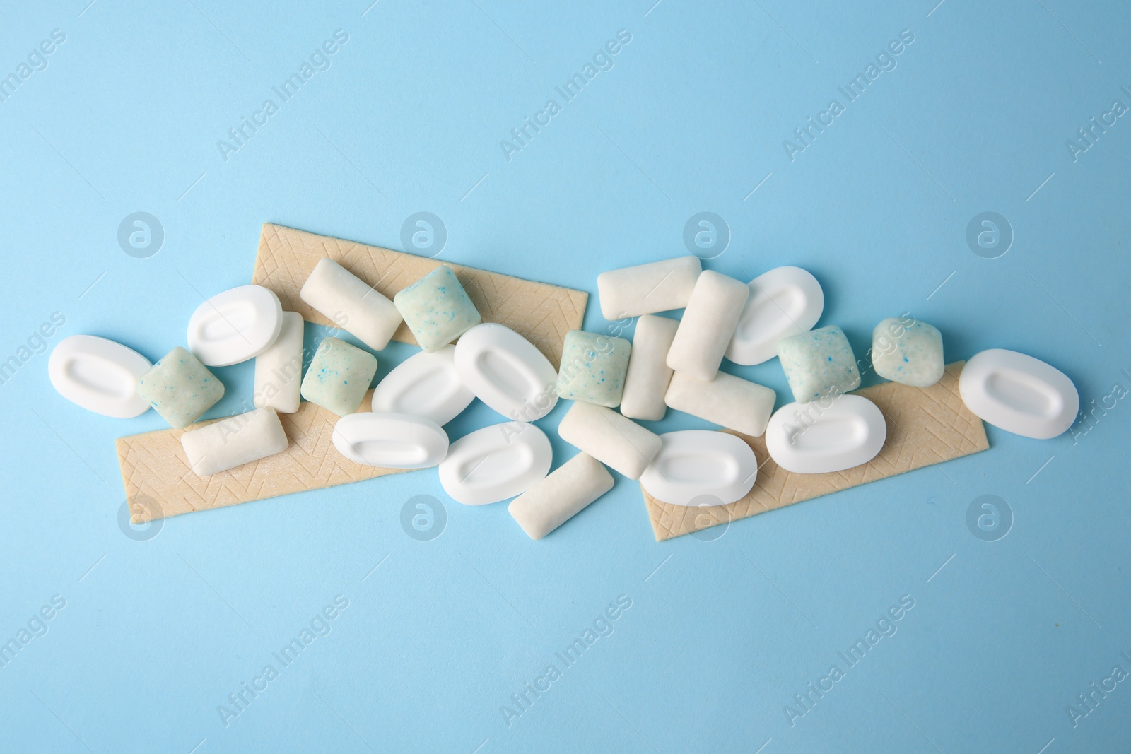 Photo of Many different chewing gums on light blue background, flat lay