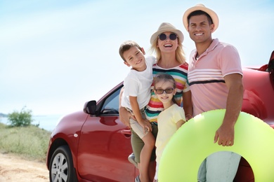 Photo of Happy family with inflatable ring near car at beach