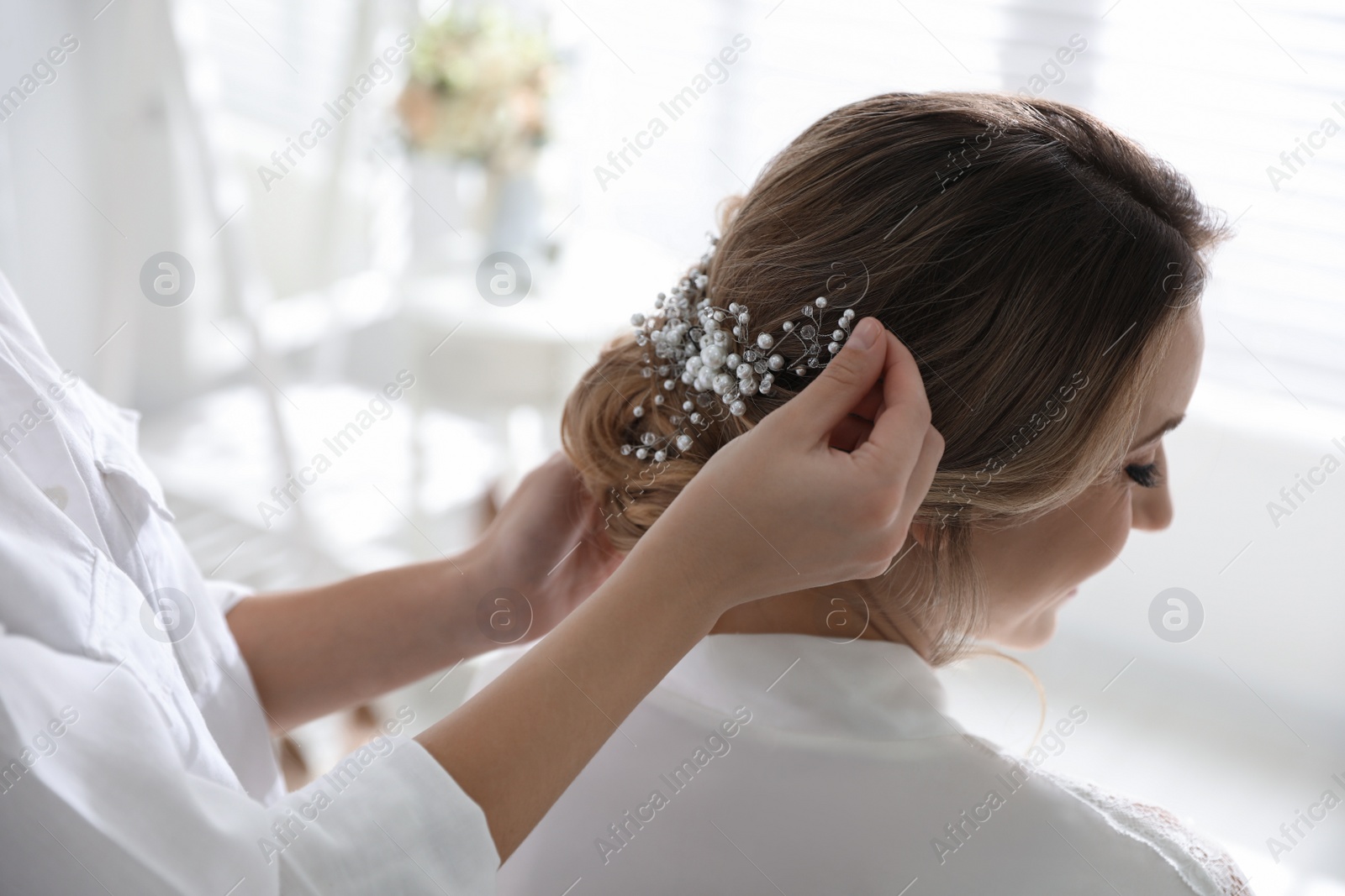 Photo of Professional stylist making wedding hairstyle for bride in salon