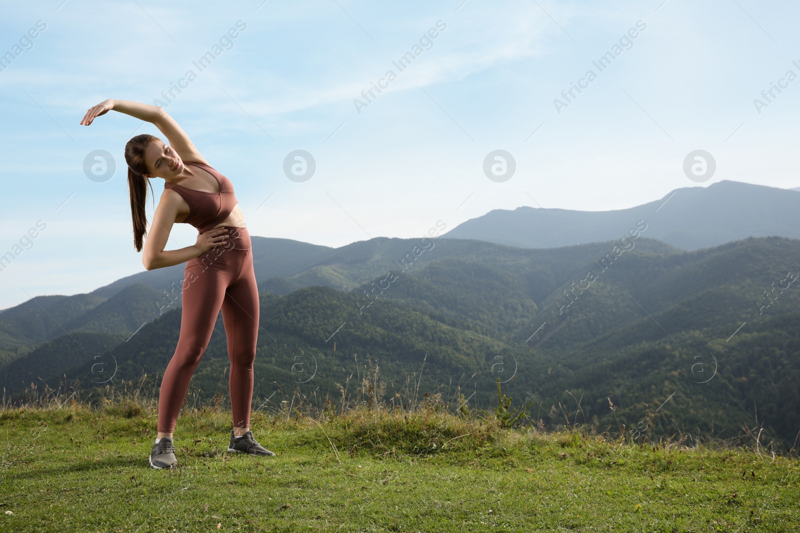 Photo of Young woman doing morning exercise in mountains, space for text