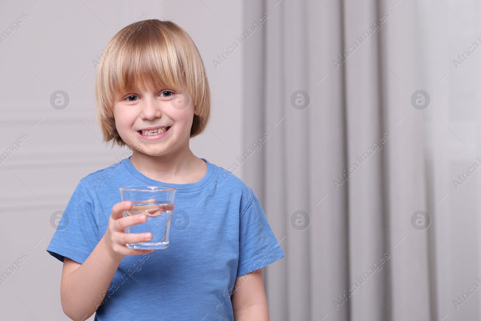 Photo of Happy little boy holding glass of fresh water at home, space for text