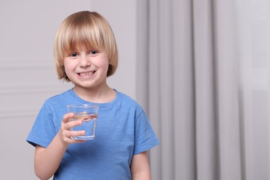 Happy little boy holding glass of fresh water at home, space for text