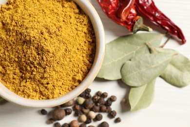 Photo of Curry powder in bowl and other spices on white wooden table, flat lay