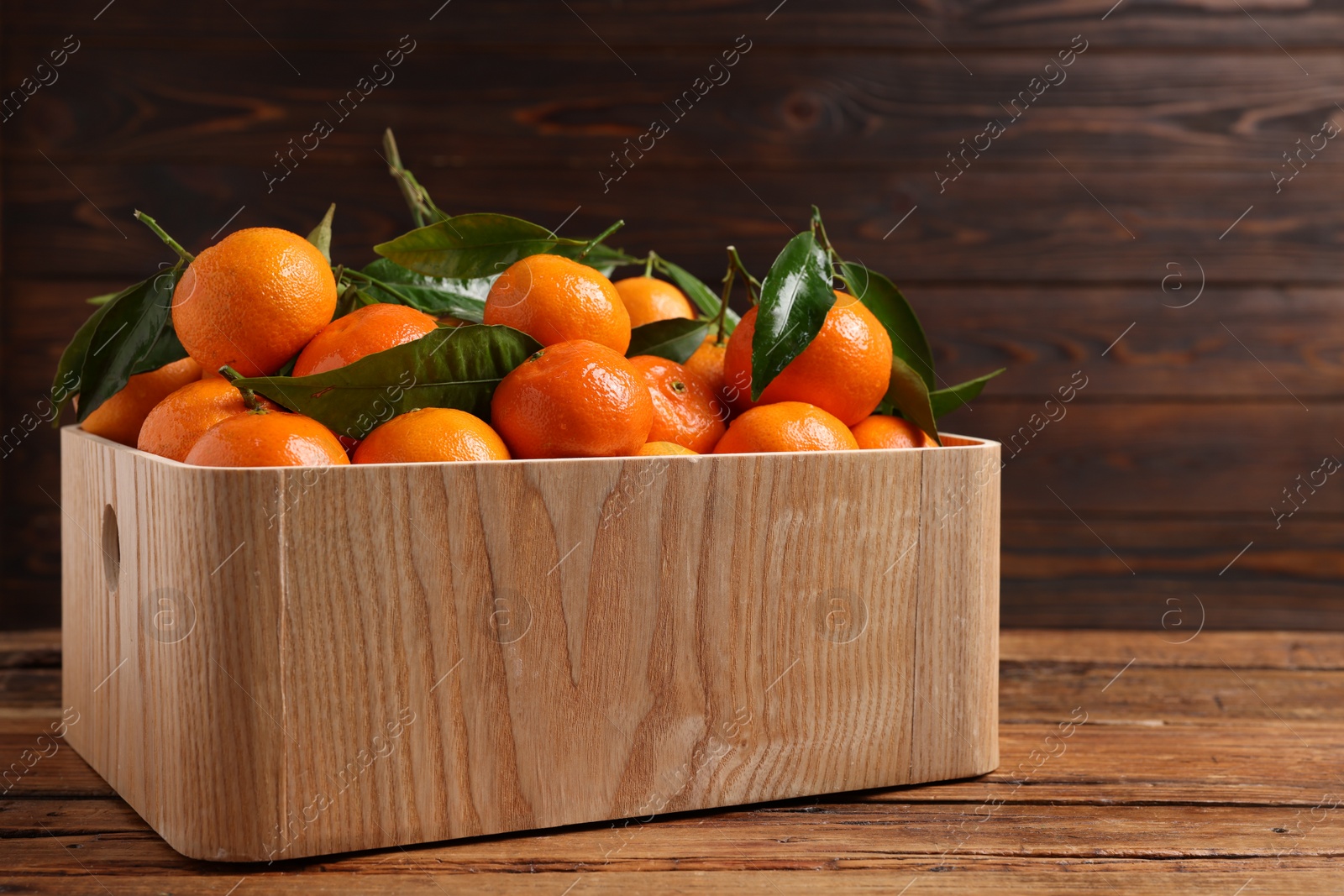 Photo of Fresh tangerines with green leaves in crate on wooden table
