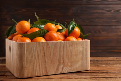 Fresh tangerines with green leaves in crate on wooden table