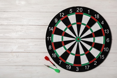 Dart board with color arrows on white wooden background, top view. Space for text