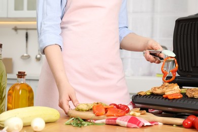 Woman cooking different products with electric grill at wooden table in kitchen, closeup