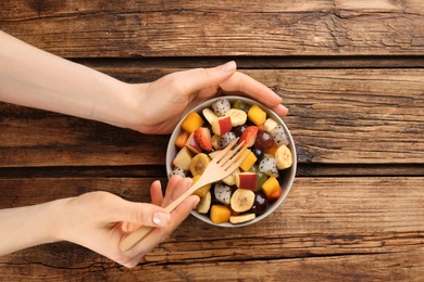 Photo of Woman with delicious exotic fruit salad at wooden table, top view