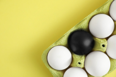 Black egg among others in box on yellow background, top view. Space for text