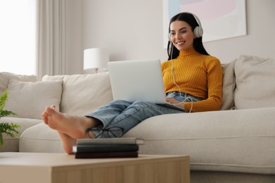 Woman with laptop and headphones sitting on sofa at home