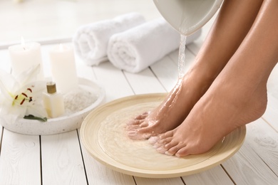 Photo of Closeup view of woman filling dish with water for foot bath indoors. Spa treatment