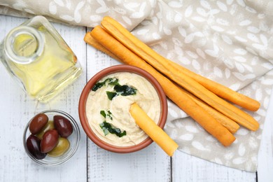 Delicious hummus with grissini sticks and olives on white wooden table, flat lay