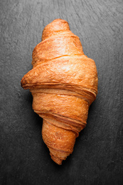 Photo of Tasty fresh croissant on black table, top view