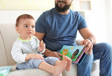 Dad reading book with his little son in living room