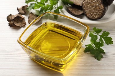Photo of Fresh truffle oil in glass bowl and parsley on white wooden table, closeup