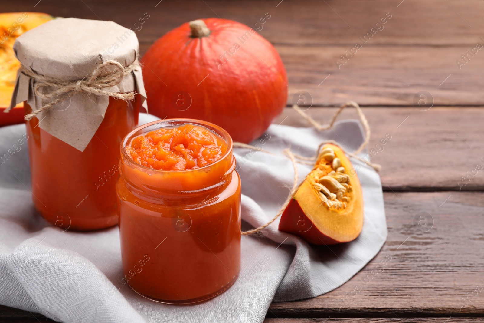 Photo of Jars of pumpkin jam and fresh pumpkins on wooden table