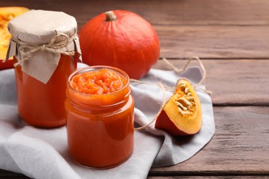 Photo of Jars of pumpkin jam and fresh pumpkins on wooden table