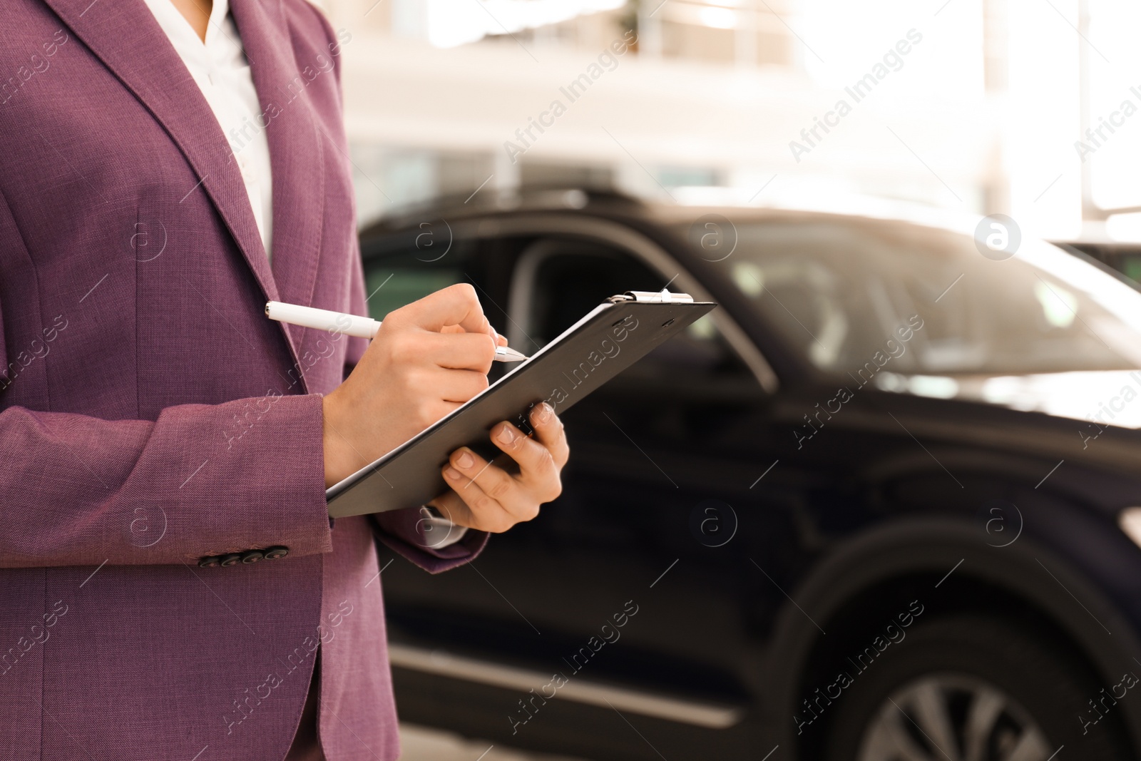 Photo of Young saleswoman with clipboard in modern car salon, closeup