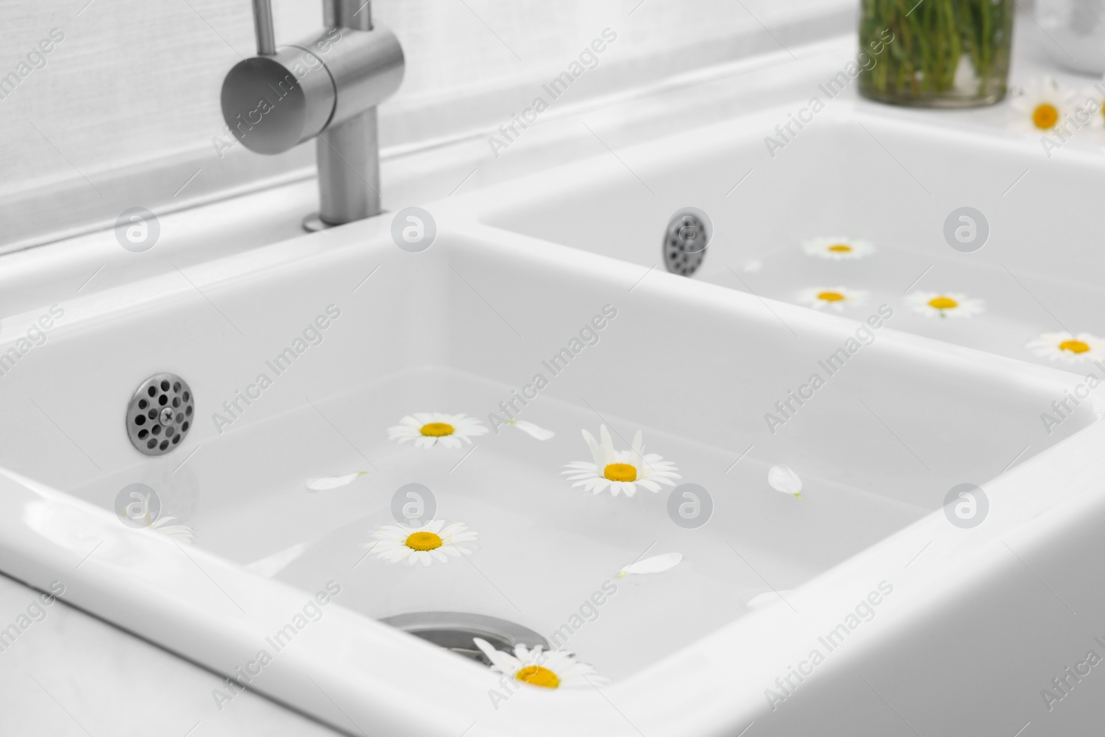 Photo of Sink with water and beautiful chamomiles indoors