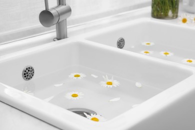 Photo of Sink with water and beautiful chamomiles indoors