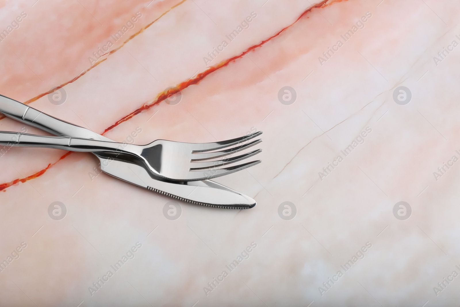 Photo of Shiny fork and knife on pink marble table, closeup. Space for text