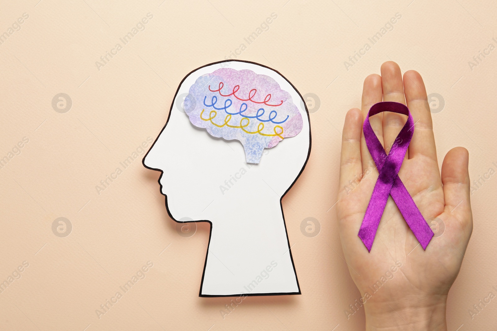 Photo of Woman holding purple ribbon near paper human head cutout over beige background, top view. Epilepsy awareness