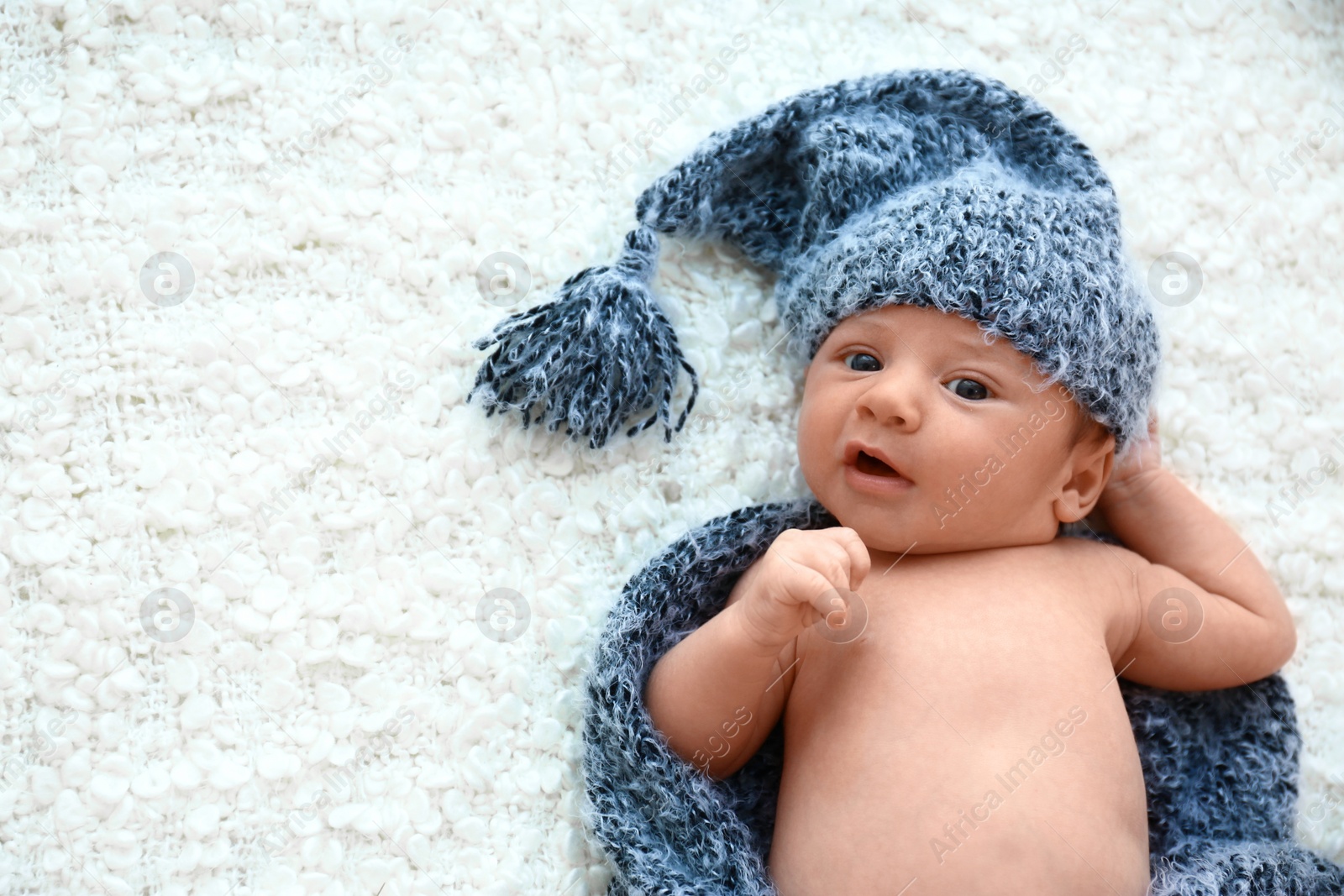 Photo of Cute little baby in grey hat and plaid lying on soft blanket, top view. Space for text