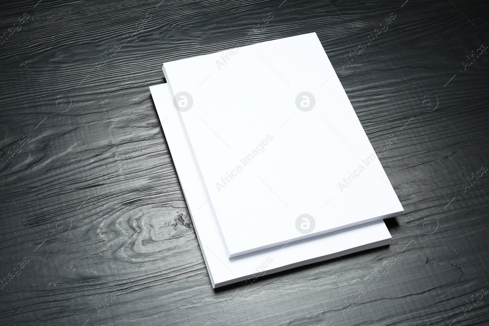 Photo of Stack of blank paper sheets for brochure on black wooden background. Mock up