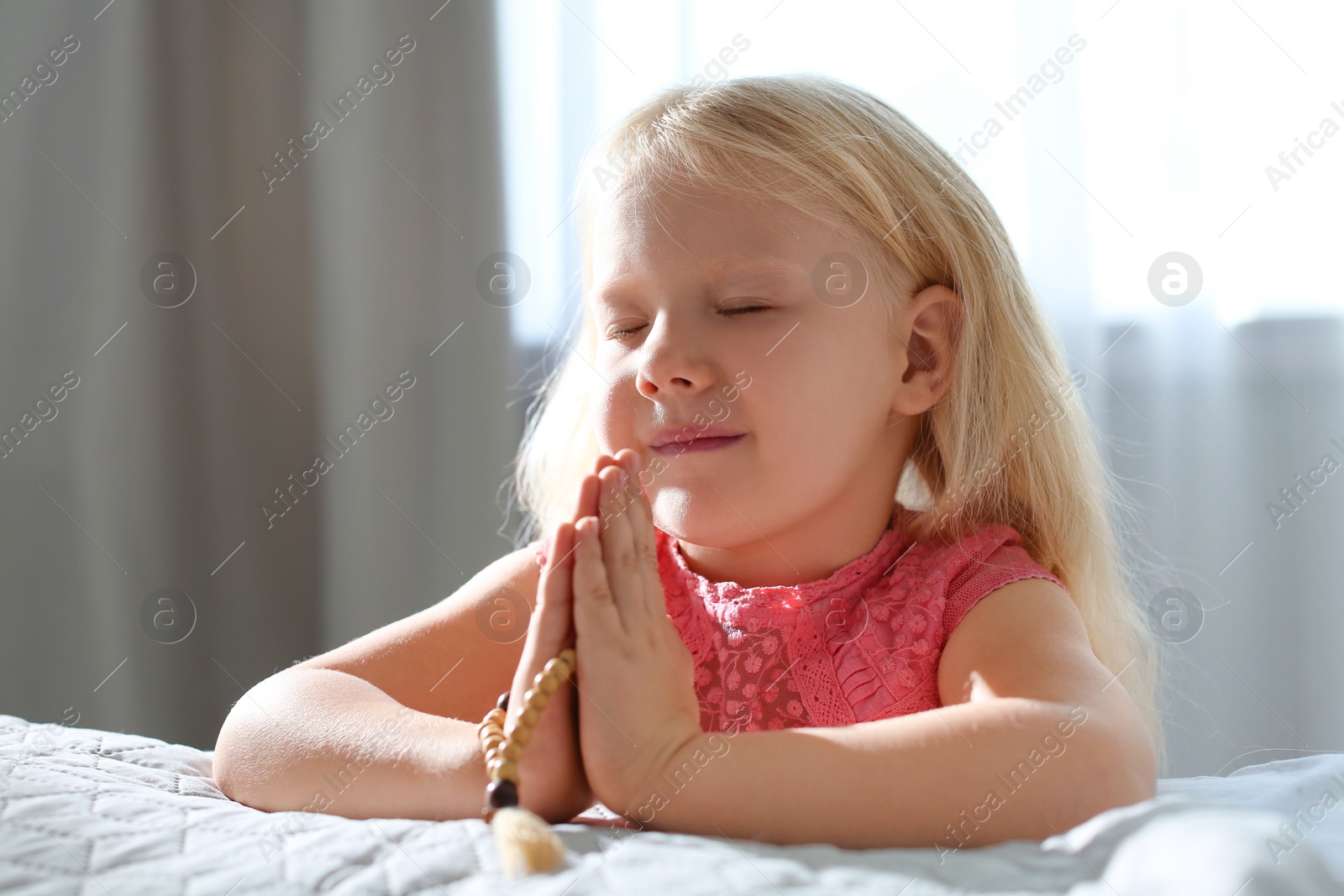 Photo of Cute little girl with beads praying in bedroom